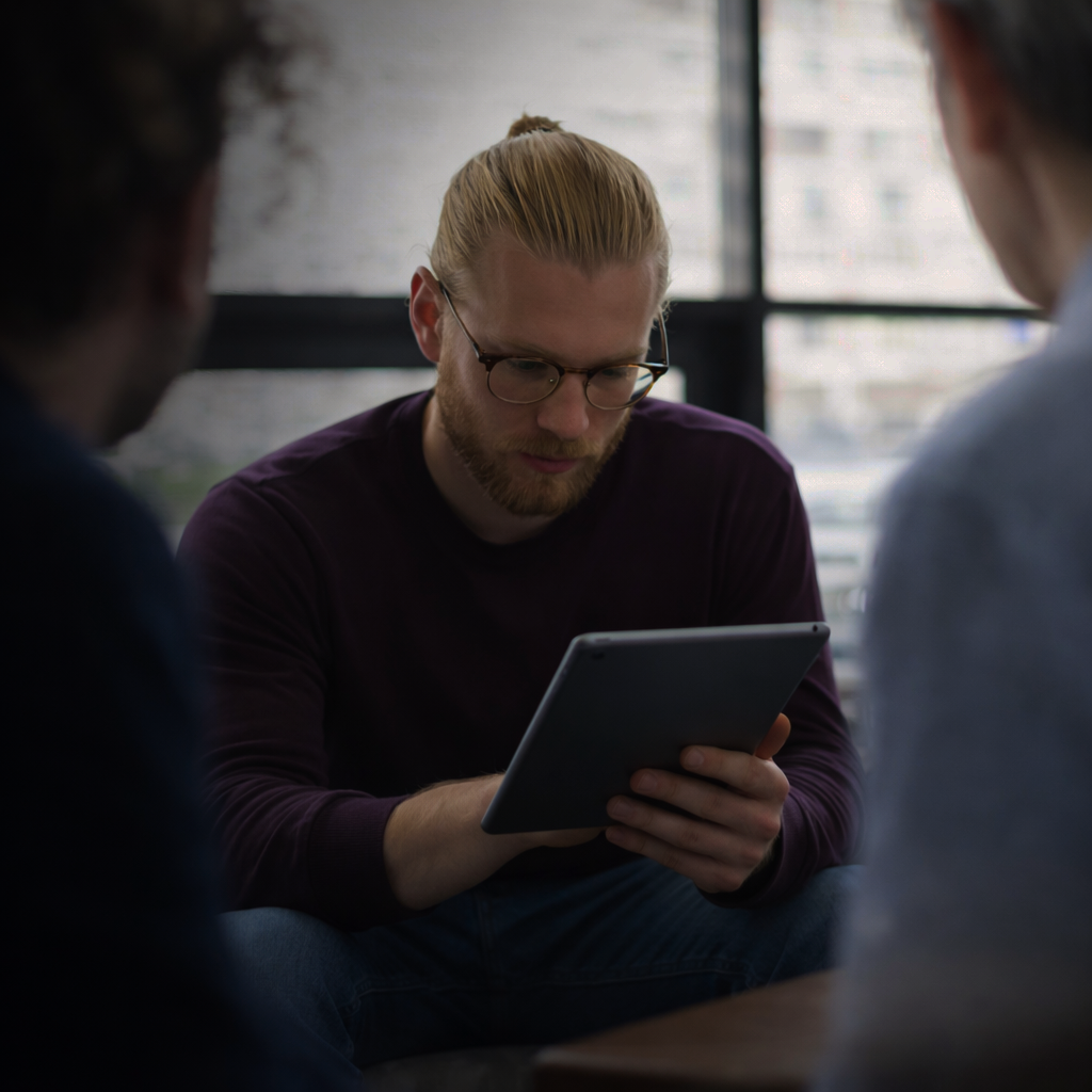 Person analysiert Informationen auf einem Tablet im Gespräch mit anderen Personen